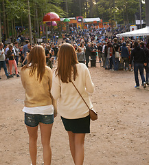 Image showing Event, festival or party with woman friends walking outdoor on ground for concert with group of people. Nature, forest or woods with young girls on sand together in audience or crowd from back