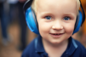 Image showing Baby, closeup and smile for portrait with headphones for noise at outdoor festival, happy and cute kid. Natural, blue and eyes with zoom face, toddler and innocent alone at concert for fun time