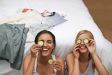 Image showing Girl friends, laughing and facial treatment with cucumber for wellness, wellbeing and self care at home. Women, fun and sitting near bed for bonding, skincare or rest and relaxation during sleepover