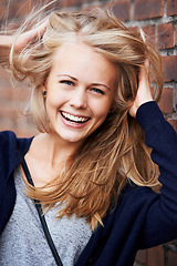 Image showing Portrait, happy and woman with wind in hair by brick wall in city, funny or laugh outdoor. Face, fashion and smile of person, stylish casual clothes and blonde girl with breeze in Switzerland