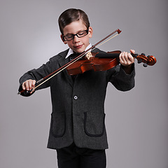 Image showing Smile, music and kid with violin in studio for practice with suit and glasses for fashion. Happy, style and cute young boy child playing string instrument with spectacles by gray background.
