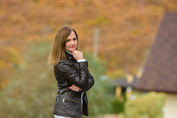 Image showing Portrait of a young beautiful girl in casual clothes against the background of a blurred autumn forest, the girl smiles and looks into the frame