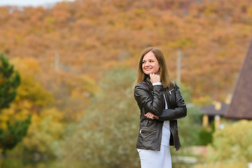 Image showing Portrait of a young beautiful girl in casual clothes against the background of a blurred autumn forest, the girl smiles and looks into the distance