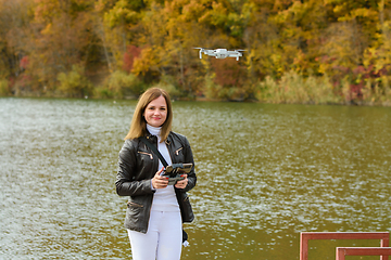 Image showing A young beautiful girl launches a radio-controlled quadcopter on the shore of an autumn lake, the girl looks into the frame