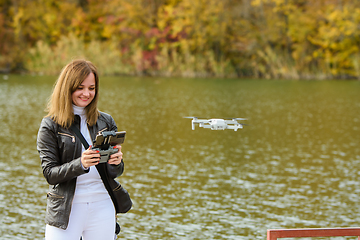 Image showing A young beautiful girl launches a radio-controlled quadcopter on the shore of an autumn lake
