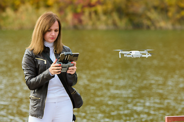 Image showing A young beautiful girl launches a radio-controlled quadcopter on the shore of an autumn lake