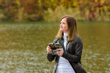 Image showing A young beautiful girl launches a radio-controlled quadcopter on the shore of an autumn lake, the girl looks at the drone