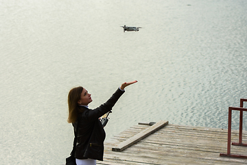 Image showing A young beautiful girl launches a radio-controlled quadcopter on the shore of a lake, the girl extended her hand to the drone