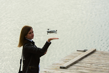 Image showing A young beautiful girl launches a radio-controlled quadcopter on the shore of a lake, the drone lands on the girl's hand