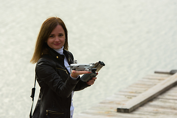 Image showing A young beautiful girl launches a radio-controlled quadcopter on the shore of a lake, the drone landed on the girl's hand