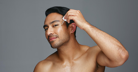 Image showing Man, face and essential oil for beauty, skincare and cosmetics product on a gray, studio background. Young asian person in portrait with facial serum, dermatology dropper or collagen for skin care