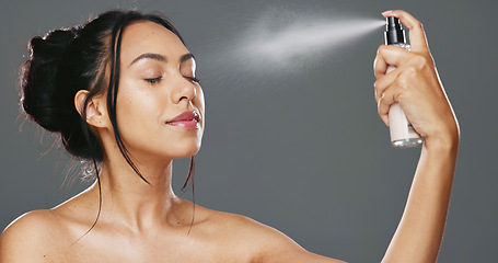 Image showing Face, woman and spray after makeup studio with product for mockup in cosmetics on gray background. Female model, happy and smile for beauty, application and facial mist on skin, hydration and glow