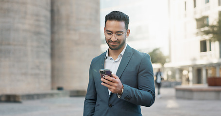 Image showing Asian businessman, mobile message and walking in city, view and confident professional in career by office buildings. Young lawyer, chat and smartphone for connection and technology in cbd in town