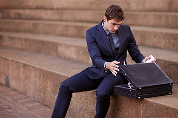 Image showing Business, briefcase and man sitting on steps outside law firm in city, outdoor commute and sidewalk of court building. Businessman, lawyer or attorney on outdoor stairs checking bag for travel.