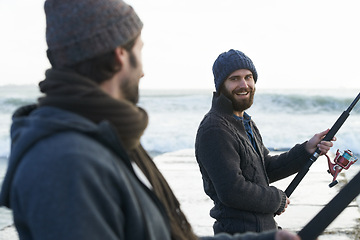 Image showing People, fishing and friends at beach for hobby, relaxing and casting a line by ocean with gear. Men, fisherman and together on vacation or holiday, happy and bonding by waves and support on adventure