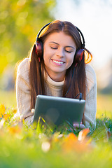 Image showing Woman, headphones and tablet for music on grass, streaming radio and online games in outdoors. Female person, nature and internet for scrolling on social media on weekend, calm and peaceful song