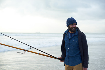 Image showing Relax, fishing and man walking on beach with rods, nature and outdoor holiday adventure. Ocean, tools and fisherman with pole, smile and cloudy sky with waves on winter morning vacation at sea.