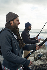 Image showing People, fishing and friends on trip at beach, relaxing and casting a line by ocean waves. Men, fisherman and cloudy sky on vacation or holiday, hobby and bonding by water and support on adventure