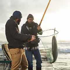 Image showing Fishing, men and net with fish at beach with rod, waves and relax on vacation, holiday and adventure. Friendship, people and bonding in morning with overcast, pier and nature for activity and hobby