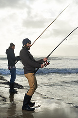 Image showing People, fishing and friends with equipment at beach, relaxing and casting a line by ocean. Men, fisherman and together on vacation or holiday, hobby and bonding by waves and support on adventure