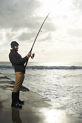 Image showing Fishing, holiday and travel with man at beach for adventure, relax and hobby break. Sunset, calm and patience with male fisherman and casting rod pole in nature for recreation, view and vacation