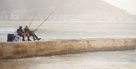 Image showing Friends, men and fishing on pier in nature with rod, water and relax on vacation, holiday and travel. Friendship, people and bonding in morning with overcast, sky and beach for activity and hobby