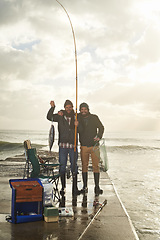 Image showing Happy, portrait and people at ocean fishing with pride to catch tuna on pier at sunset. Fisherman, friends and smile holding fish in hand on adventure in nature at sea for holiday or vacation