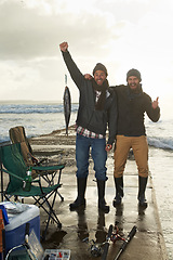 Image showing Happy, portrait and men fishing at beach with pride for tuna catch on ocean pier at sunset. Fisherman, friends and smile holding fish in hand in nature at sea on holiday, adventure or vacation