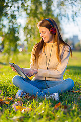 Image showing Woman, headphones and relaxing with music on tablet, streaming radio and podcast in outdoors. Female person, nature and internet for classical playlist on weekend, calm and peaceful song on grass