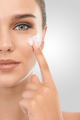 Image showing Woman, skincare and cream in studio portrait, hydration and proud of glow on white background. Female person, half face and apply lotion for treatment, luxury cosmetics and moisturizer for soft skin