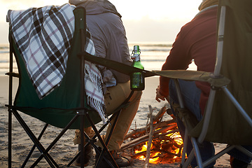 Image showing Beer, beach and man friends by fire on sand by ocean or sea together for travel, holiday or vacation. Nature, relax and people drinking on coast from back with view of sunset, horizon and coast