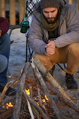 Image showing Campfire, wood and men by beach for travel on vacation, adventure or holiday camping. Nature, outdoor and young male people sitting on chair in sand with flame for heat on weekend trip in winter.