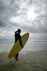 Image showing Man, surfboard and adventure at beach on vacation, weekend and sports for fitness in water. Male person, back and cloudy sky for ocean waves, wetsuit and traveling on holiday or getaway for peace