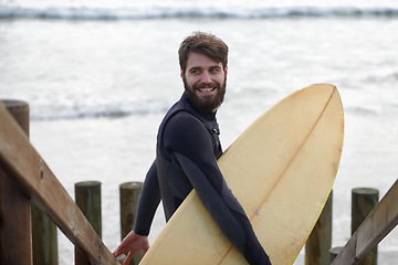 Image showing Happy man, surfer and beach by waves for fitness, exercise or extreme sports on outdoor shore. Young male person with smile and surfboard for surfing challenge or hobby at ocean coast, sea or nature