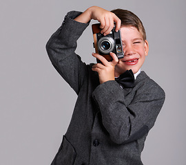 Image showing Camera, photography and boy child in studio in elegant, classy or fancy suit outfit with smile. Happy, vintage and young kid with dslr equipment for picture with bowtie for fashion by gray background