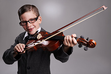 Image showing Smile, music and child with violin in studio for practice with suit and glasses for fashion. Happy, style and portrait of young boy kid play string instrument with spectacles by gray background.