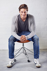Image showing Man, portrait and smile on chair with fashion on wall background for style, confidence or relax. Male person, face and sitting or casual in jeans in studio for happiness in Canada, clothes or outfit