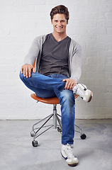 Image showing Man, portrait and smile on chair with style on wall background for fashion, confidence or relax. Male person, face and sitting or casual in jeans in studio for happiness in Canada, clothes or outfit