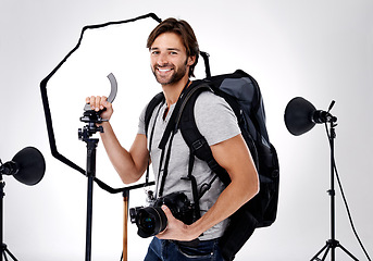 Image showing Photographer, backpack and happy with camera in studio for career, behind the scenes and equipment. Photography, person or smile with lighting, confidence and shooting gear for photoshoot or passion