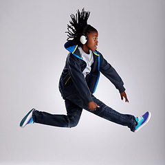 Image showing Black child, jump and headphones for fashion in studio for hiphop in backdrop of white background. Boy, funky and happiness of skilled performer with smile of youth for kids clothes and dance