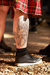 Image showing Closeup, man and leg with tattoo, outdoor and festival with sneakers and weekend break. Person, outside and guy with a shoes and summer for fun and getaway trip with art and ground with sunshine