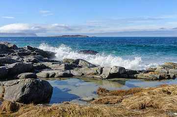 Image showing Waves crashing on rocky shoreline under blue sky during daytime