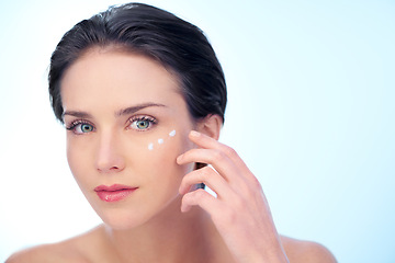 Image showing Woman, portrait and moisturizer application on face for smooth skincare for treatment, dermatology or wellness. Female person, model and lotion on blue background in studio, mockup space or product