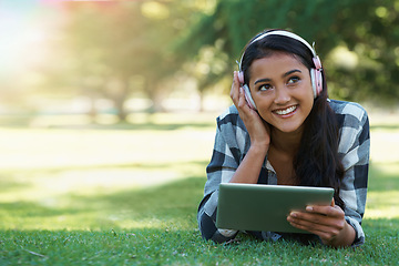 Image showing Woman, headphones and streaming podcast on tablet, learning and internet for education on grass in outdoors. Female person, happy and relaxing on lawn, knowledge and student subscription for info