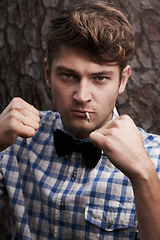 Image showing Fight, smoking and portrait of man in outdoors for challenge, strong and fighting. Cigarette, hipster and anger with face of male person and hands up in nature for combat, cool and trendy style