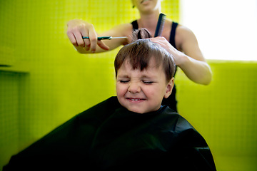 Image showing Kid, boy and hairdresser with haircut at salon for grooming, hairstyle and grimace with scissors. Barber, person and child for hair treatment, haircare and hairdressing with comb, happy and grimace