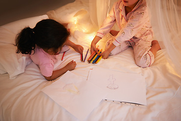 Image showing Girls, color pencil and drawing on bed for sleepover, creative and relax in bedroom for weekend. Young kids, playing or educational toys at night in pajamas, friends or bonding by fairy light in home