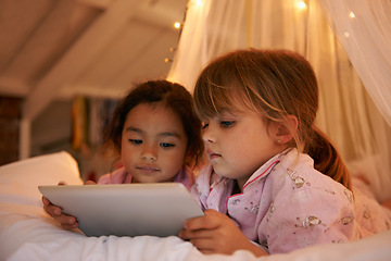 Image showing Girls, tablet or games on bed at night, playing or digital technology for cartoons with love in home. Young kids, friends or connection by fairy light, tent or streaming video for bonding together