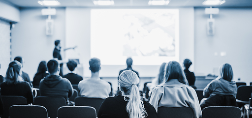 Image showing Speaker giving a talk in conference hall at business event. Rear view of unrecognizable people in audience at the conference hall. Business and entrepreneurship concept. Blue tones black and white.