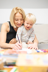 Image showing Caring young Caucasian mother and small son drawing painting in notebook at home together. Loving mom or nanny having fun learning and playing with her little 1,5 year old infant baby boy child.